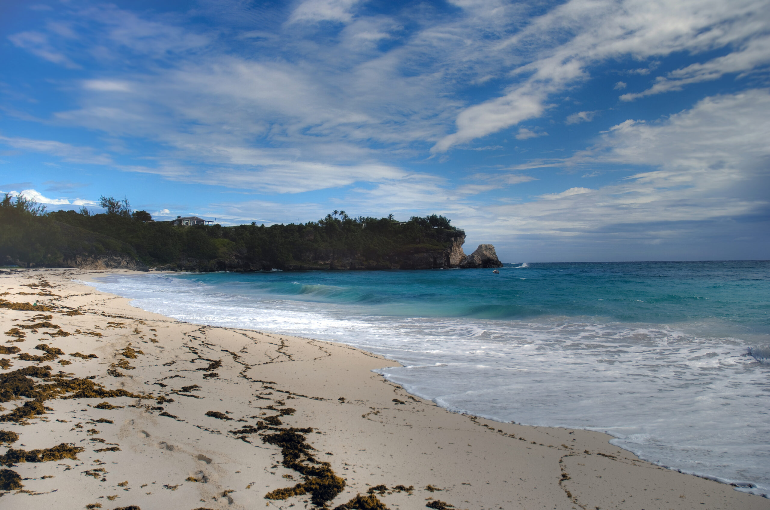 Wide sandy beach in Barbados with turquoise Caribbean water, white surf, rocky headland and blue sky
