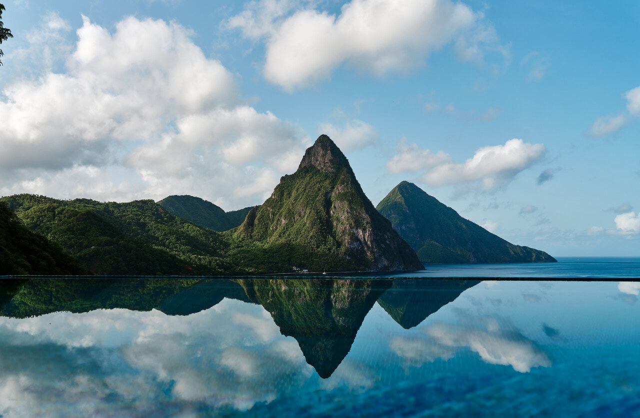 Saint Lucia's Petit Piton and Gros Piton rising above the Caribbean Sea and reflected in calm water beneath a blue sky