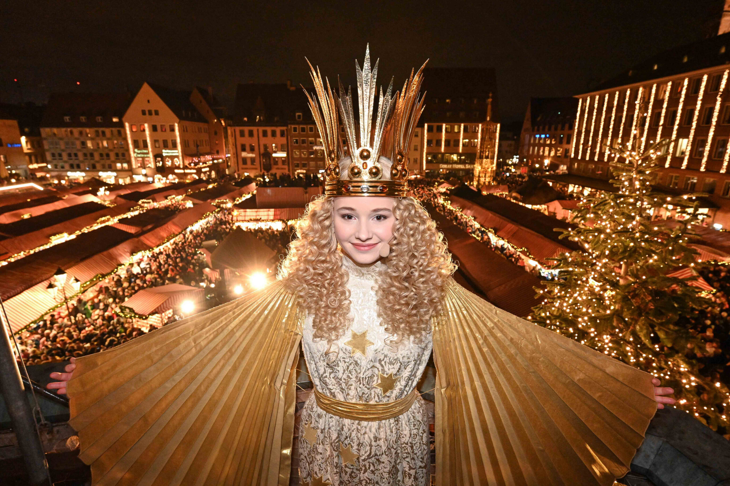 Nuremberg Christkind at the illuminated Christkindlesmarkt with rows of festive market stalls and Christmas lights behind her