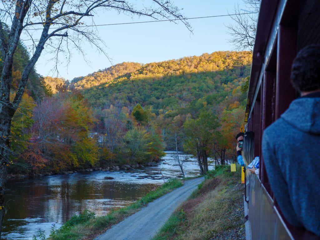 Great Smoky Mountains Railroad train viewed beside a river and colorful Appalachian fall foliage